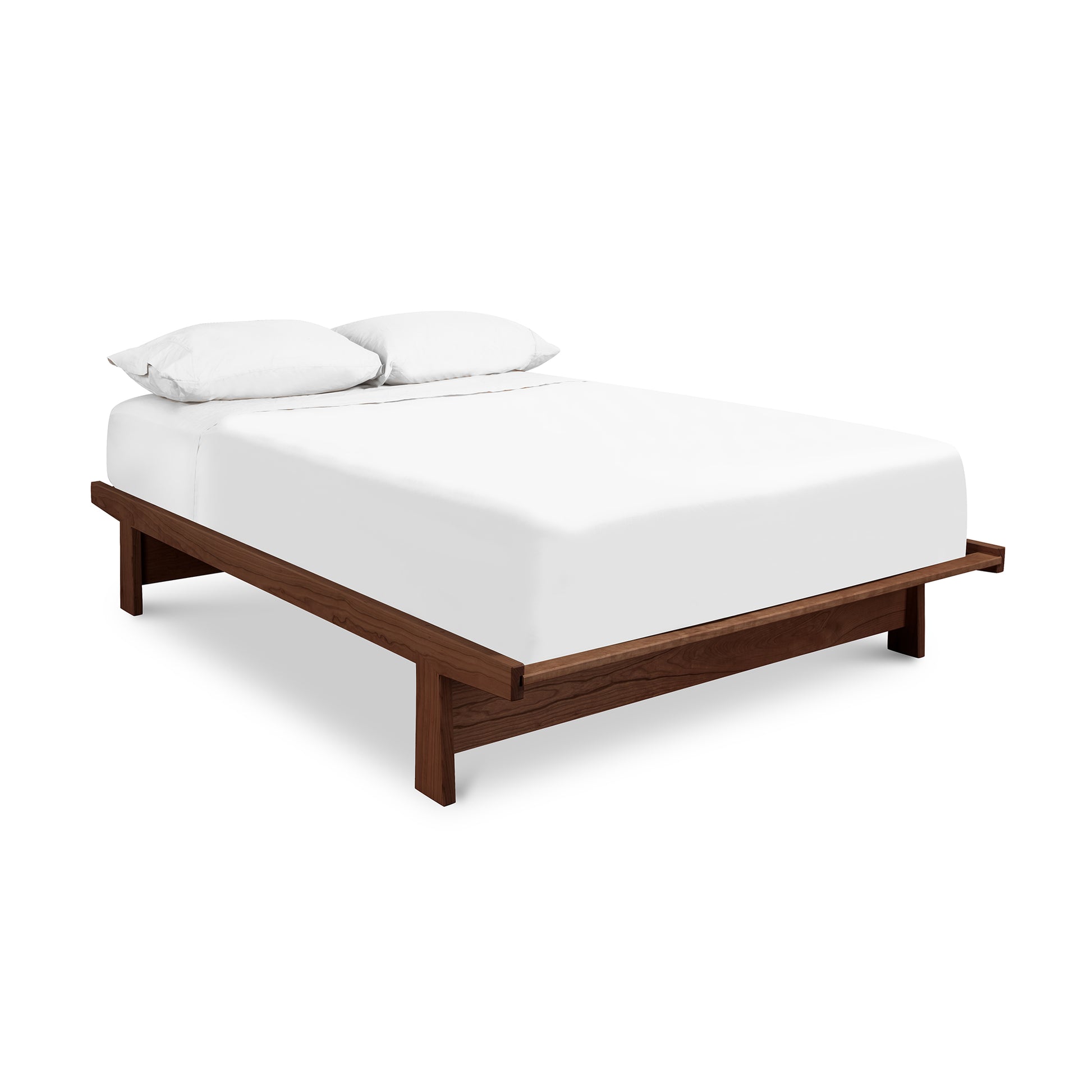 A Cherry Moon Dovetail Platform Bed by Maple Corner Woodworks with an eco-friendly oil finish, and a white mattress with two pillows, isolated on a white background.