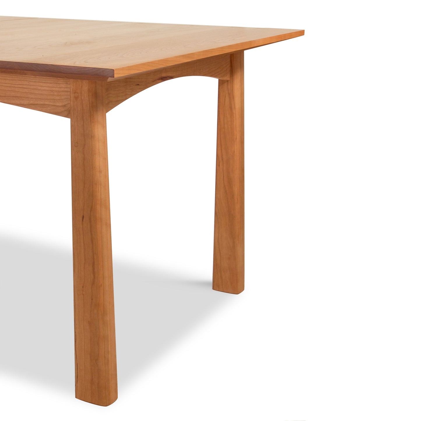 A simple Arts & Crafts style Cherry Moon Extension Dining Table with a smooth top and sturdy legs, shown against a white background, with its corner facing the viewer, by Maple Corner Woodworks.