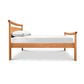 A single Maple Corner Woodworks Cherry Moon Pagoda Bed made of natural cherry hardwood, with a white mattress and a pillow, isolated on a white background with slight shadowing beneath the bed.