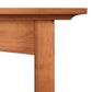 Close-up view of a Maple Corner Woodworks Cherry Moon Solid Top Dining Table showing the top surface and a part of the leg, highlighting the wood grain texture and warm brown tone.