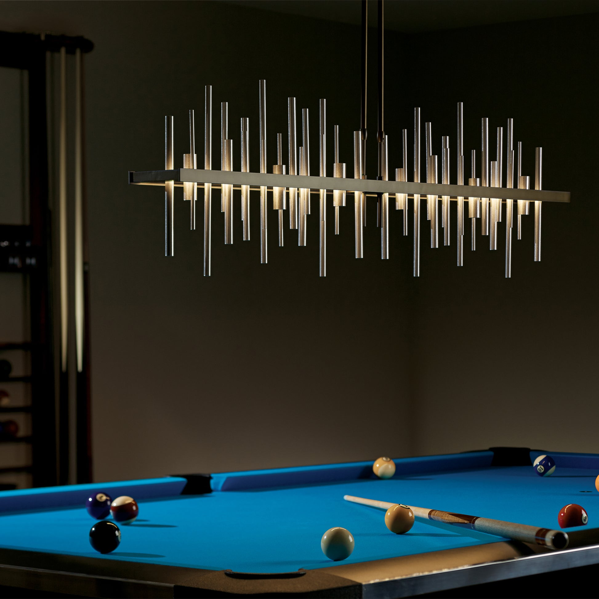 In a dark room, a pool table is illuminated by the warm glow of the Hubbardton Forge's Cityscape Large LED Pendant. The sleek and modern design adds an urban panorama feel to the space.