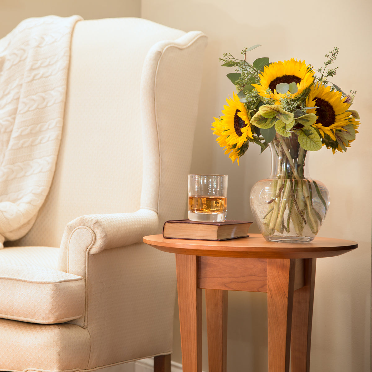 Lyndon Furniture Classic Shaker Round Flare Leg End Table next to a beige armchair, showcasing American made hardwood craftsmanship.
