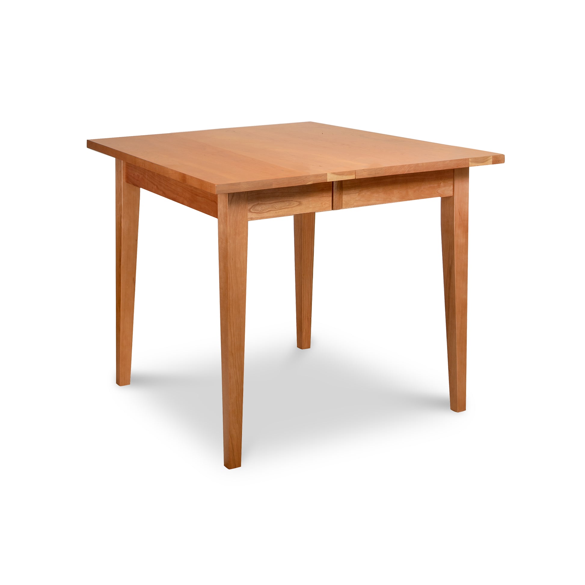 The Classic Shaker Square Extension Table by Lyndon Furniture is a square wooden table with a light brown finish, handcrafted in Vermont. It features four straight legs and has a minimalist design, showcasing the elegance of sustainably sourced hardwoods.