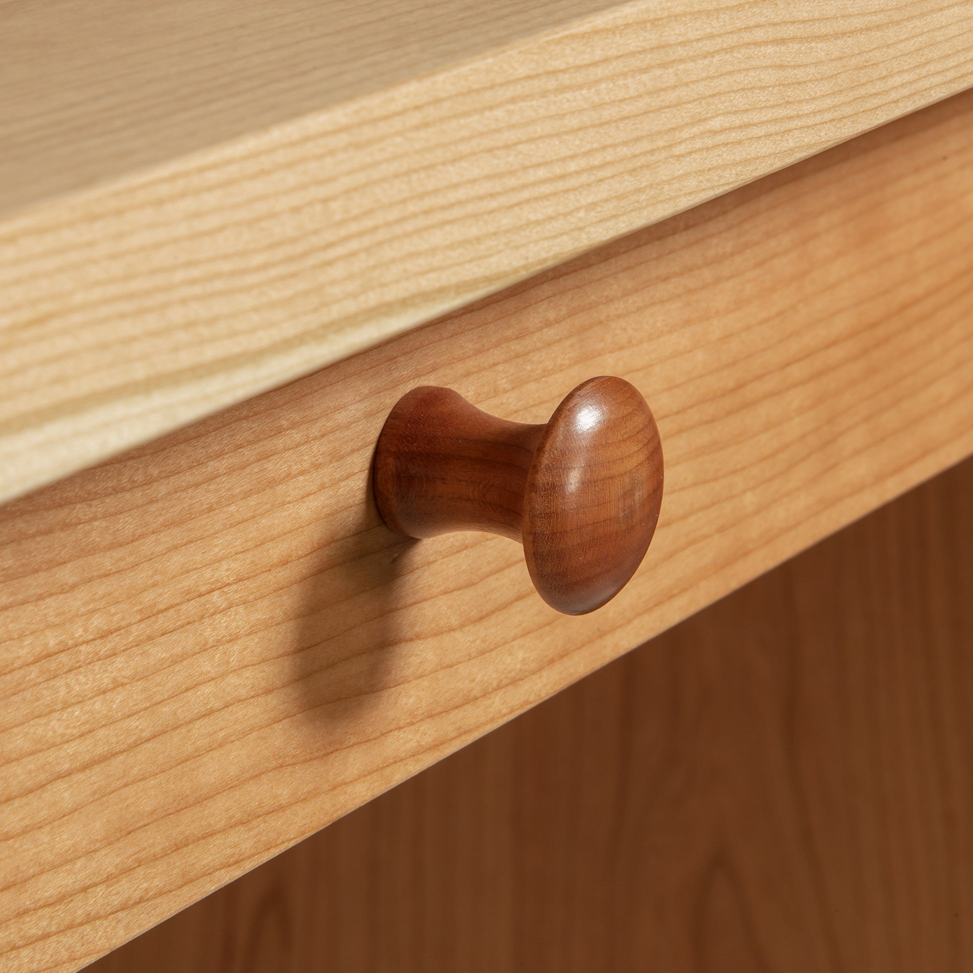 Close-up of a solid wood drawer in the Lyndon Furniture Small Executive Desk with a round wooden knob. The light to medium cherry wood finish highlights the natural grain texture, emphasizing high quality, American made craftsmanship.