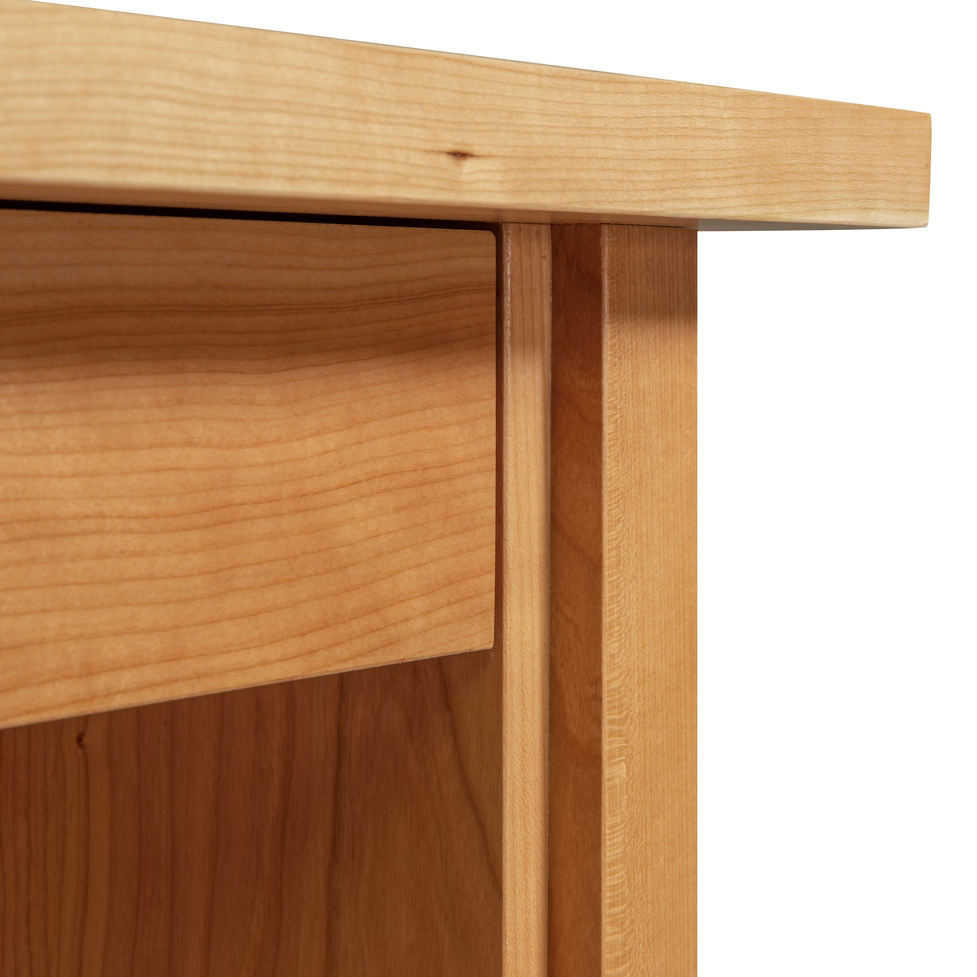 Close-up of the edge of a solid cherry wood table by Lyndon Furniture, showcasing exquisite craftsmanship with polished grain patterns. The image highlights the top surface, side, and leg detail of this American-made Small Wood Executive Desk from Vermont Woods Studios.