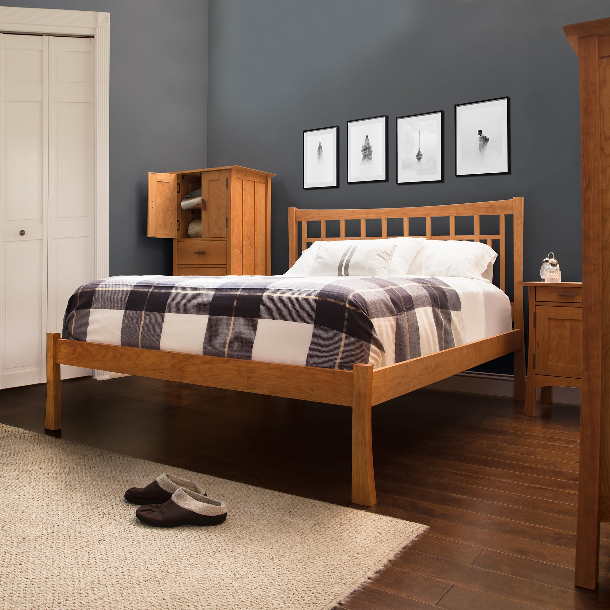 A neatly made bed with a checkered patterned comforter in a bedroom with dark blue walls and a Contemporary Craftsman Low Footboard Bed by Vermont Furniture Designs, accompanied by matching wooden furniture and wall art above the bed.