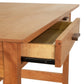 A wooden Vermont Furniture Designs Contemporary Craftsman Writing Desk with an open drawer showing a metal runner and dovetail joints.