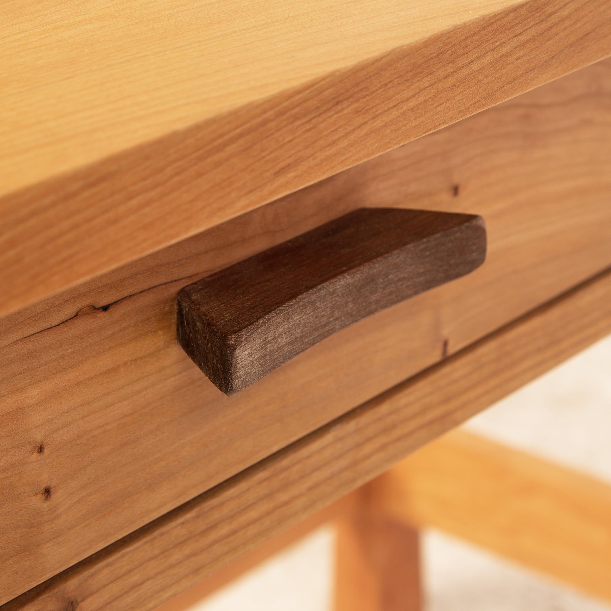 A close-up image of a wooden drawer from a Vermont Furniture Designs Contemporary Craftsman Writing Desk, with a simple, rectangular pull handle featuring Arts and Crafts styling.