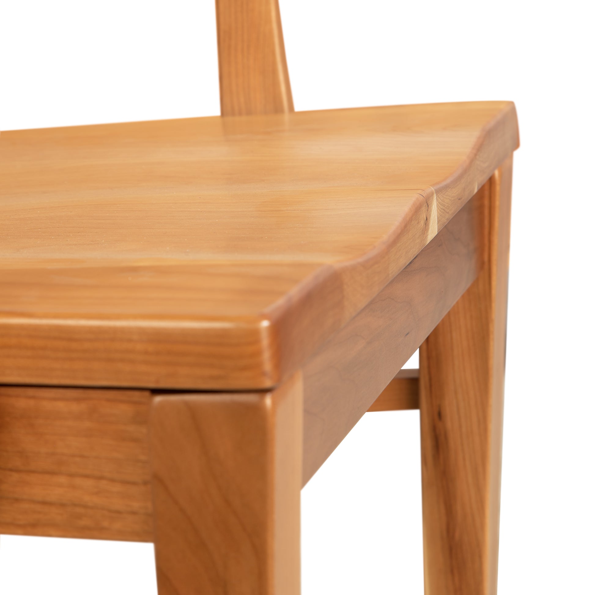 Close-up of a Vermont Woods Studios Contemporary Shaker Chair with Wood Seat, focusing on its scooped seat and part of the backrest, showing details of the wood grain and finish against a white background.