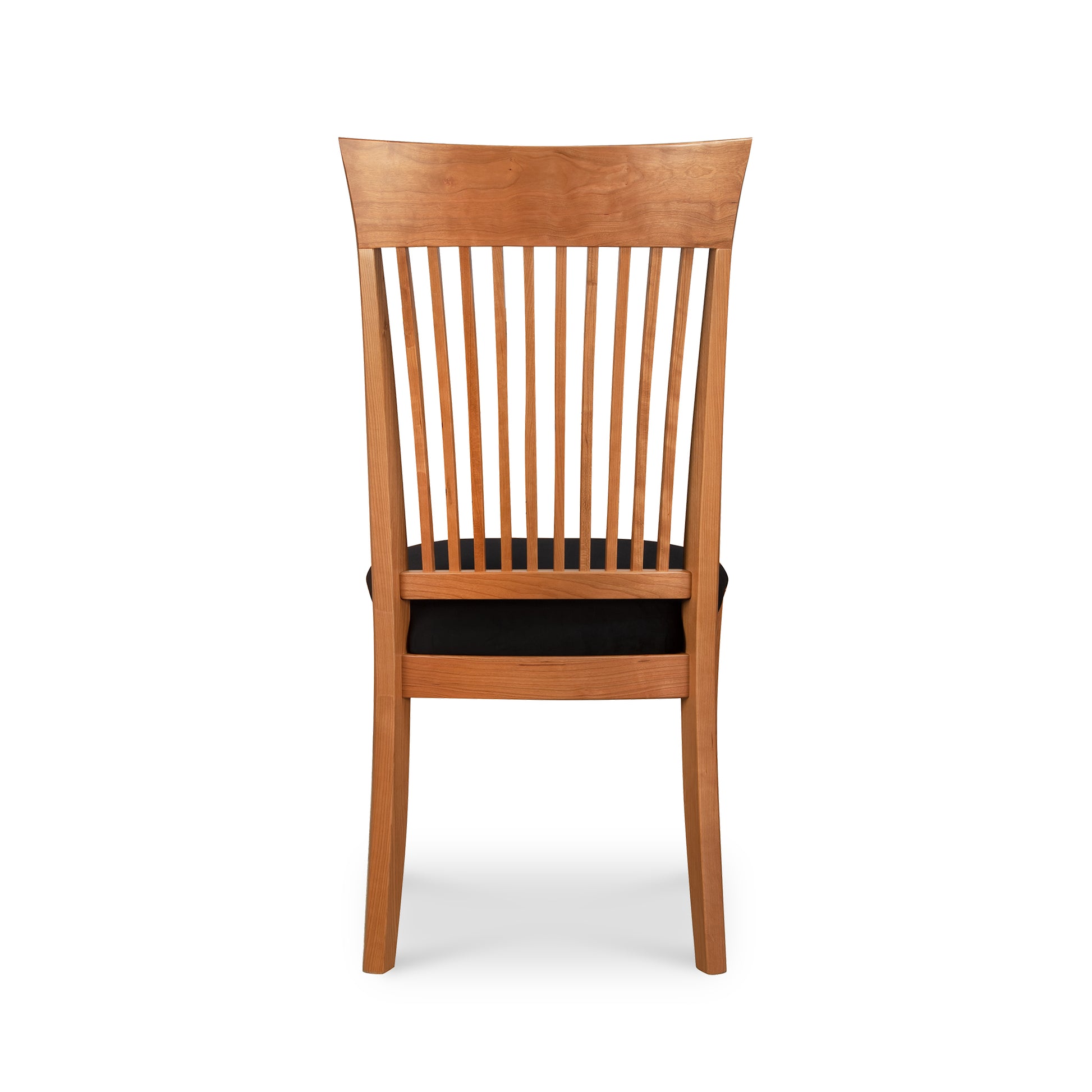 The view shows a Vermont Woods Studios Contemporary Shaker Side Chair with Black Upholstery - Display Model from directly behind, highlighting its sustainably handcrafted design. The dining chair features a high, slightly curved backrest composed of multiple vertical slats, a padded seat covered in black fabric, and boasts a natural wood finish with simple, clean lines reminiscent of classic Shaker Chairs.