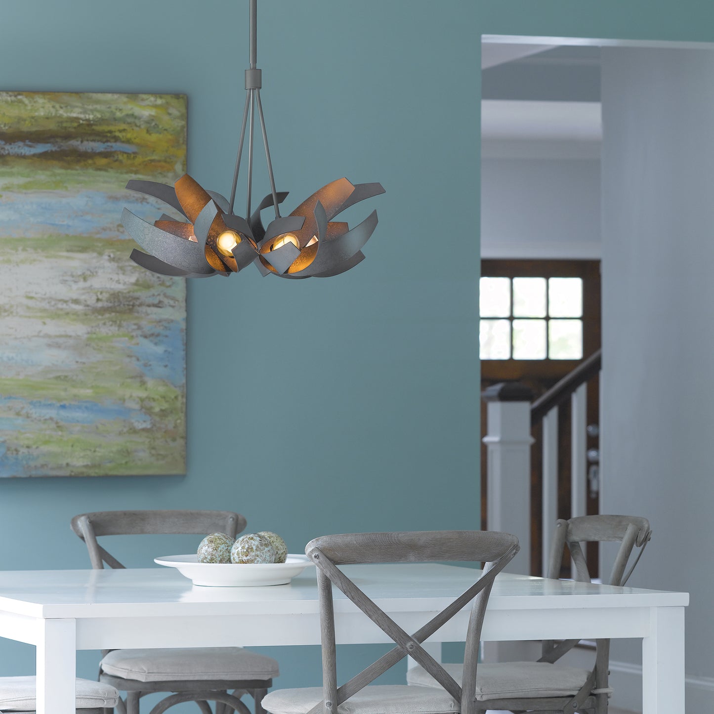 A dining room with blue walls and a white table and chairs featuring a designer pendant, the Hubbardton Forge Corona Pendant.