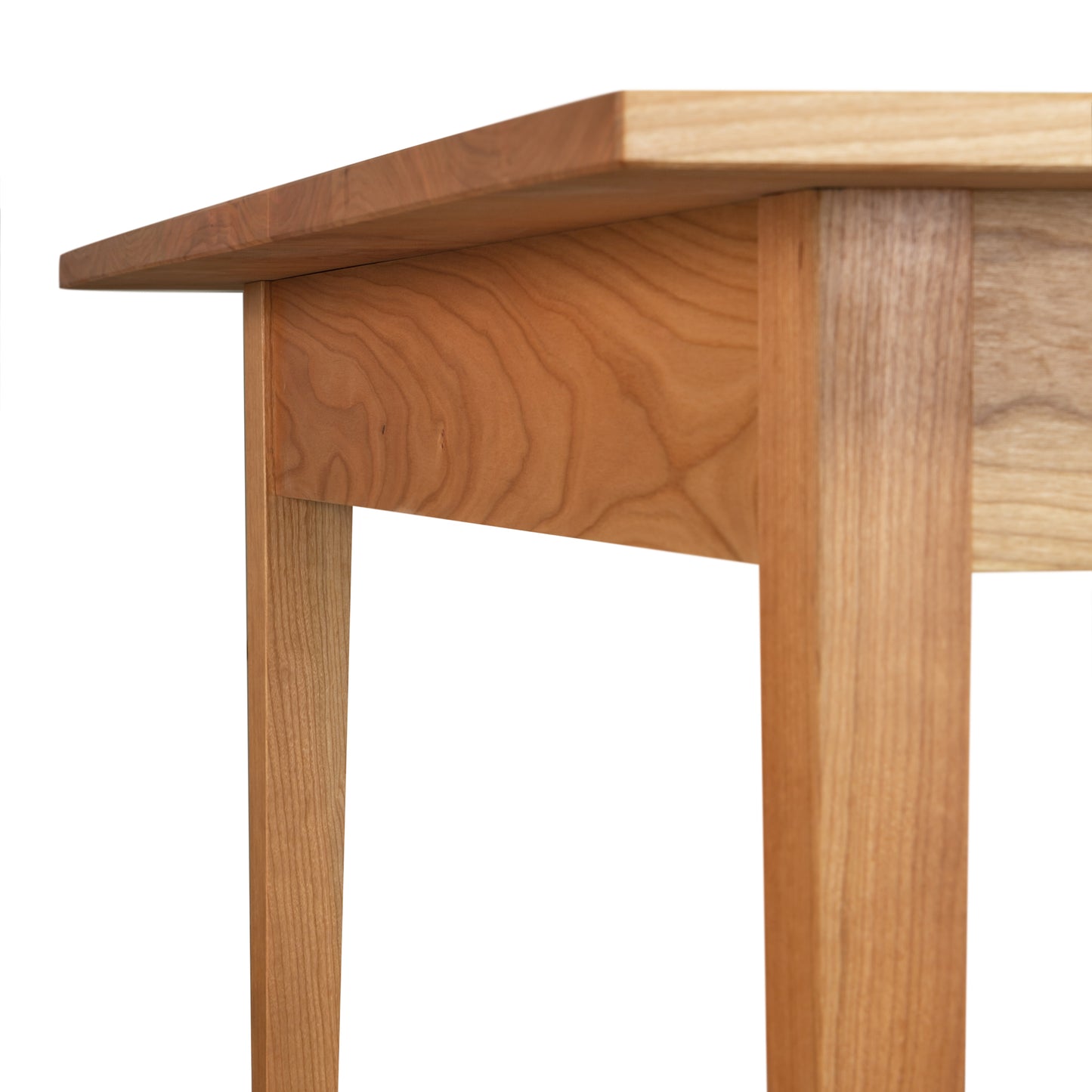 Close-up of the corner of a wooden table by Vermont Woods Studios. The image focuses on the legs and underside of the natural wood top, showcasing its light, natural finish and smooth design. The grain is visible. This customizable Country Shaker Dining Table - 36"x60" stands against a plain white background and is a discontinued design that is ready to ship.