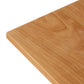 A close-up view of the corner of a Vermont Woods Studios Country Shaker Dining Table in the 36"x60" discontinued design, showcases its smooth, polished surface and natural grain patterns. The light brown natural wood top has a slight sheen, and the straight, well-defined edges add to its refined appearance. This table is ready to ship.