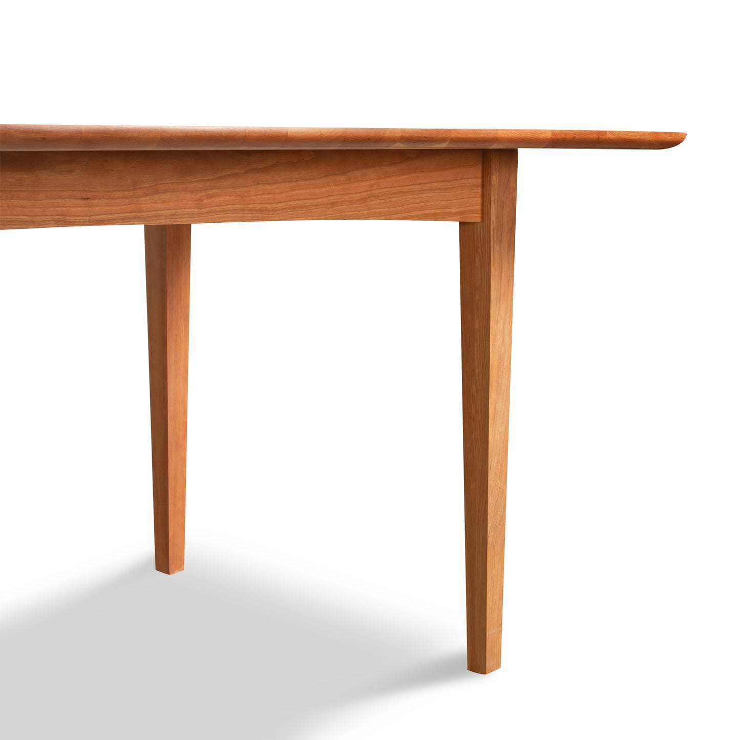 A Custom Heartwood Shaker Extension Dining Table from Vermont Furniture Designs is shown. The table, with a rectangular top and four straight legs, is made of solid maple wood and features an eco-friendly oil finish. It is photographed against a white background, with only a portion of the table visible in the image.