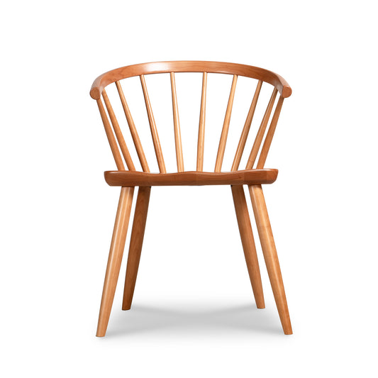 The Dover Curveback Windsor Chair - Display Model by Vermont Woods Studios is a wooden dining chair that boasts a curved spindle back and four straight legs. Its minimalist design features smooth lines and a natural wood finish. Made from sustainable solid wood, the flat seat and ergonomic backrest with multiple vertical slats fan outward for added comfort.