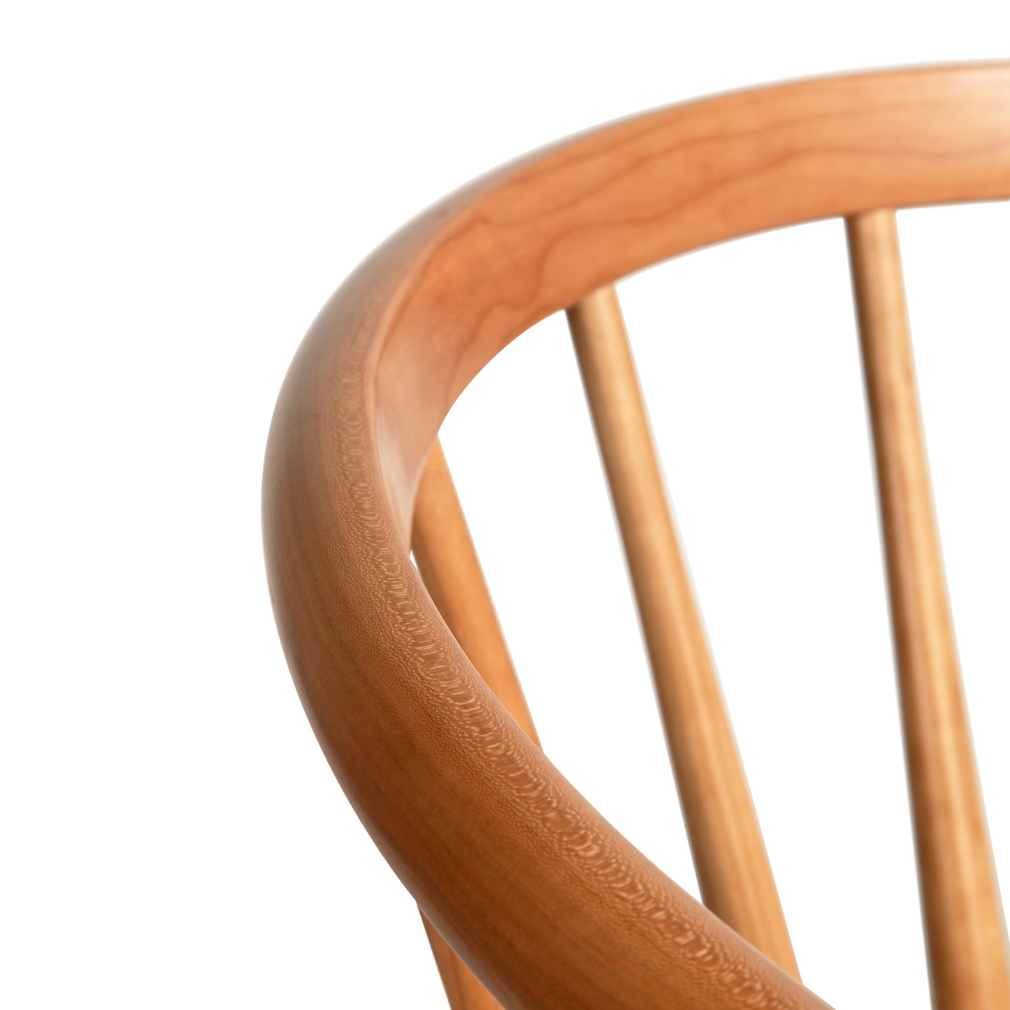 Close-up of the top part of a Dover Curveback Windsor Chair by Vermont Woods Studios, featuring a smooth, curved backrest and evenly spaced vertical slats. The light, natural wood finish adds a contemporary Windsor-style look.