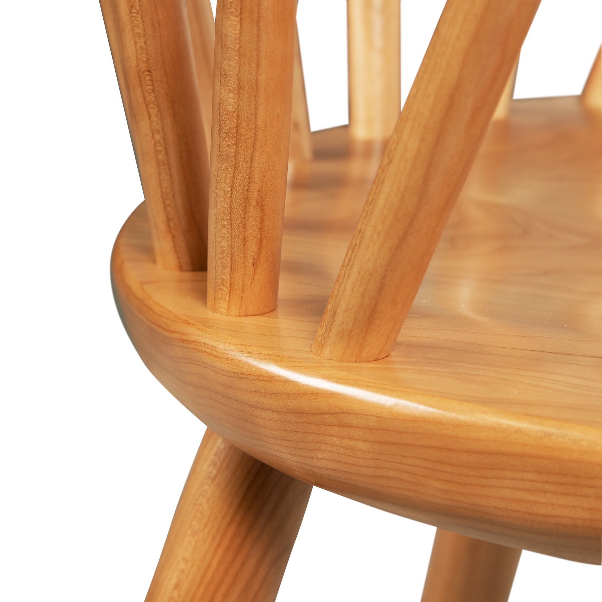 Close-up image of the seating area of a Dover Curveback Windsor Chair - Display Model by Vermont Woods Studios. The chair features a rounded seat with vertical backrest slats, showcasing a smooth, polished finish with visible wood grain, embodying a traditional Windsor-style design.