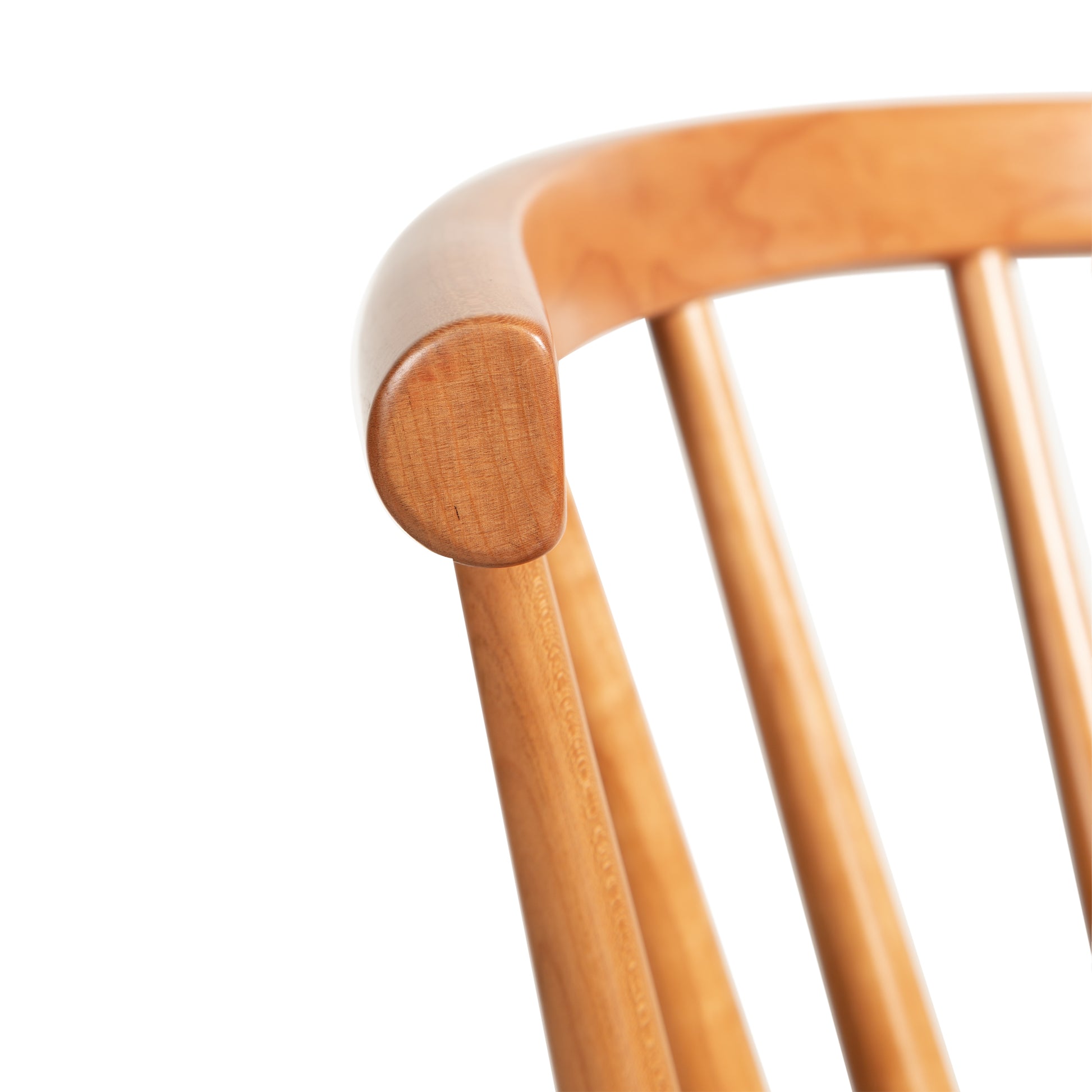 Close-up of the upper back section of the Dover Curveback Windsor Chair by Vermont Woods Studios. The chair features a smooth, rounded top rail and evenly spaced vertical slats, capturing the essence of contemporary Windsor-style with its polished, light, warm finish.