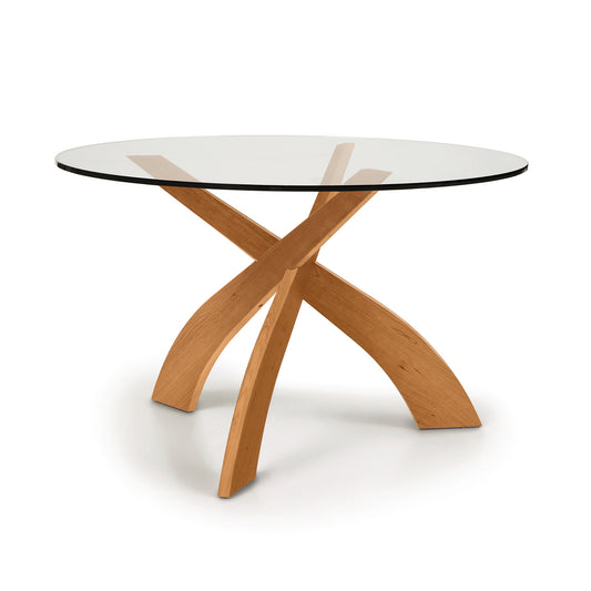 Entwine Round Glass Top Dining Table by Copeland Furniture with a tempered glass top and a sustainably sourced cherry wood cross base on a white background.