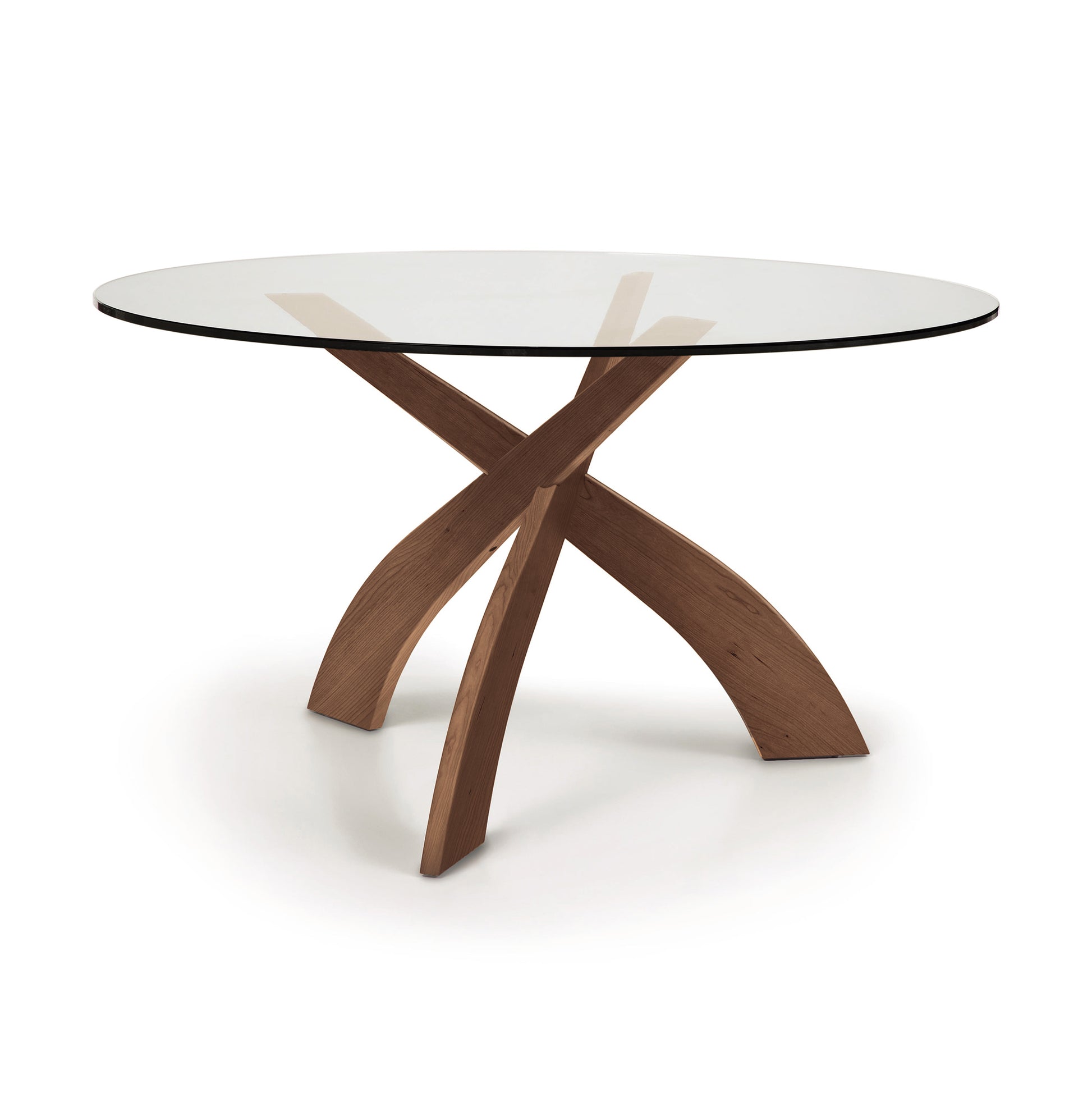 A modern Entwine Round Glass Top Dining Table by Copeland Furniture with a sustainably sourced cherry wood cross-type base on a white background.