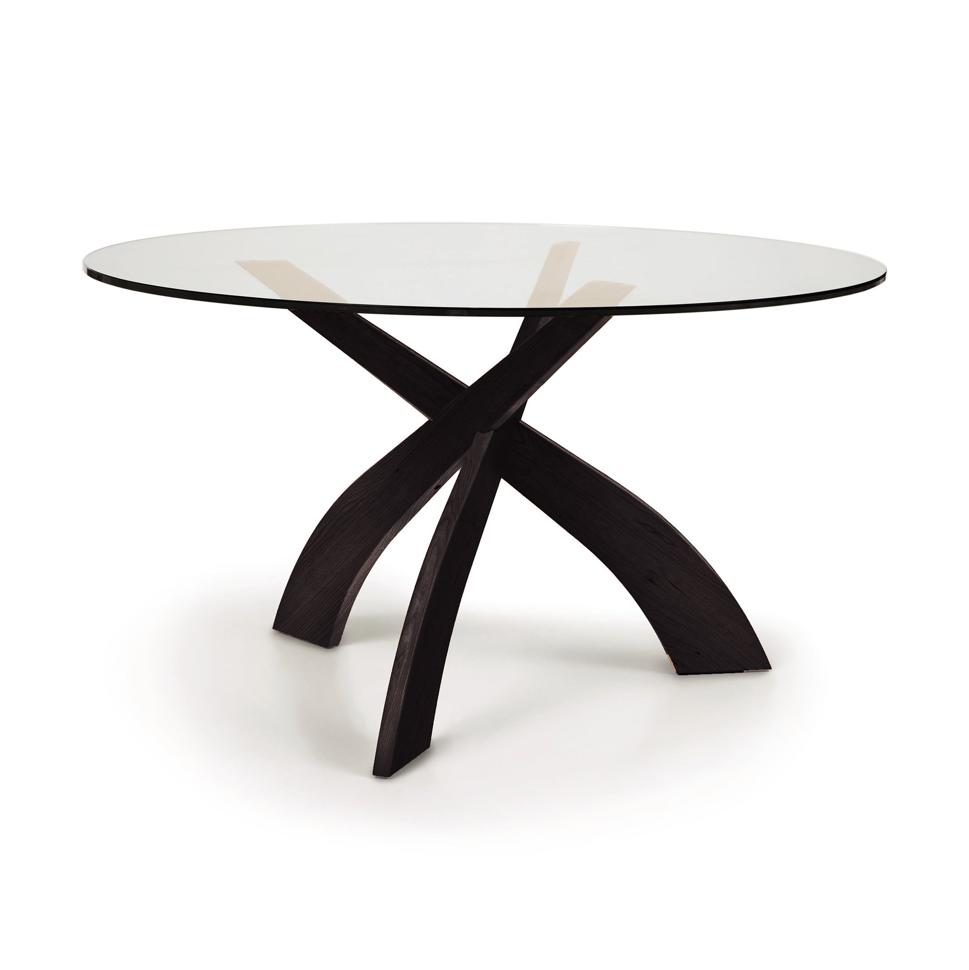 A Entwine Round Glass Top Dining Table with a dark sustainably sourced cherry wood base featuring intersecting legs on a white background.