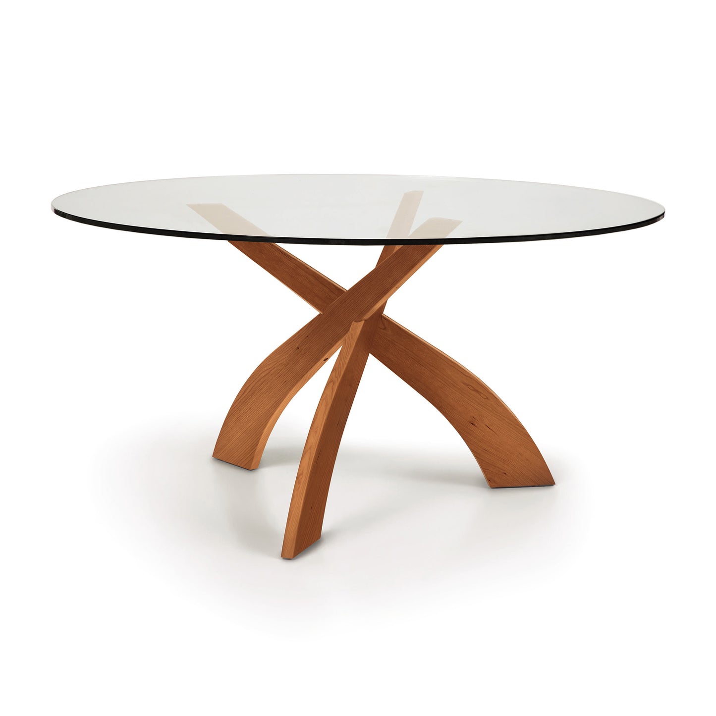 A modern Entwine Round Glass Top Dining Table with a tempered glass top and a sustainably sourced cherry wood x-shaped base by Copeland Furniture.