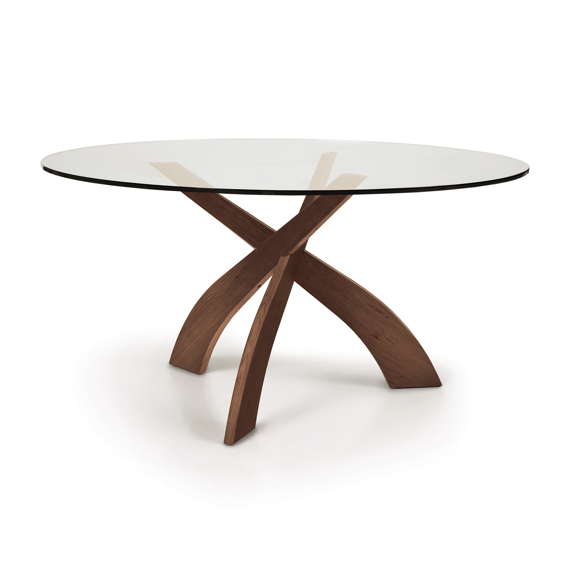 A Entwine Round Glass Top Dining Table, from Copeland Furniture, supported by a sustainably sourced cherry wood cross-shaped base, isolated on a white background.