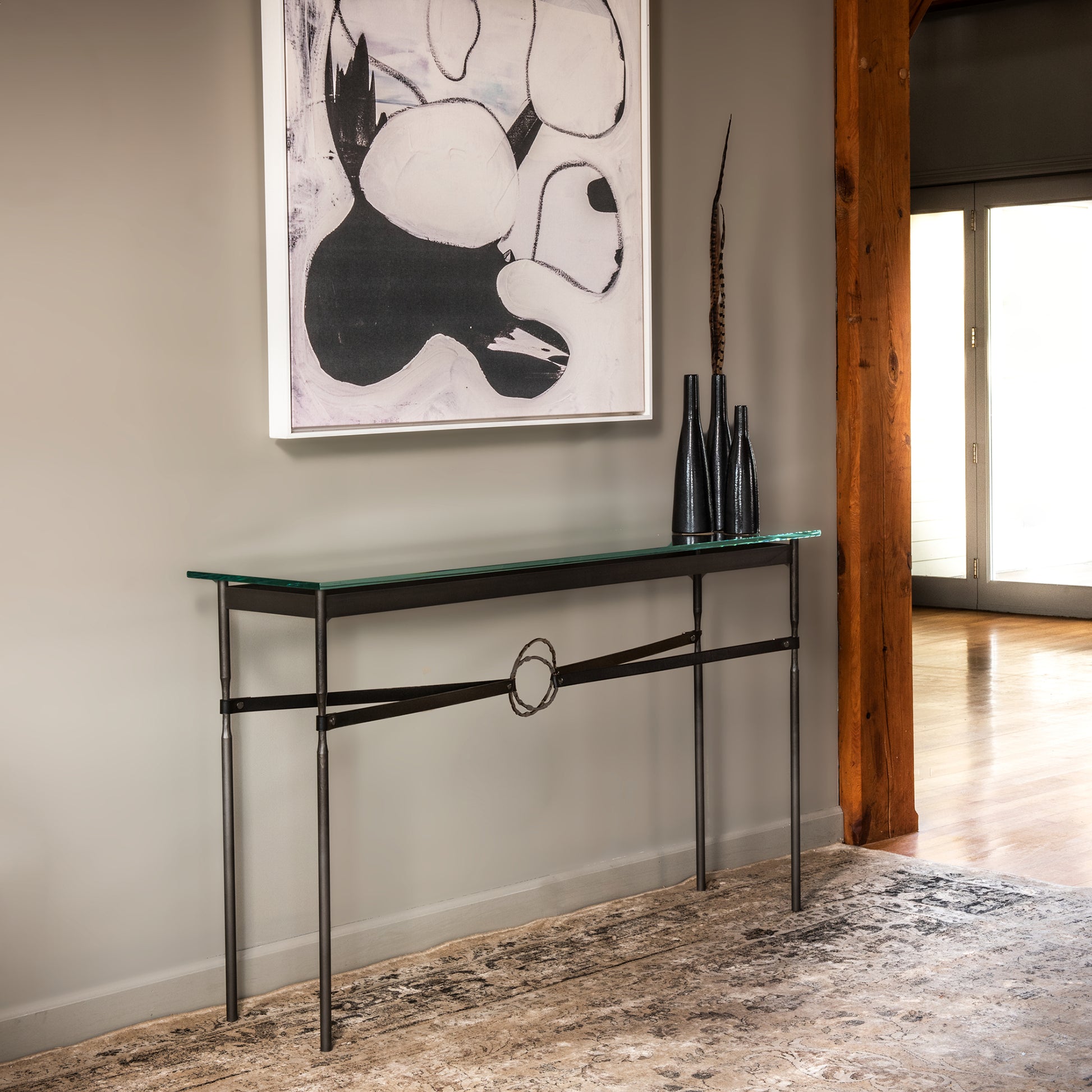 An artisanal-made Equus Console Table by Hubbardton Forge in a room with a painting on the wall.