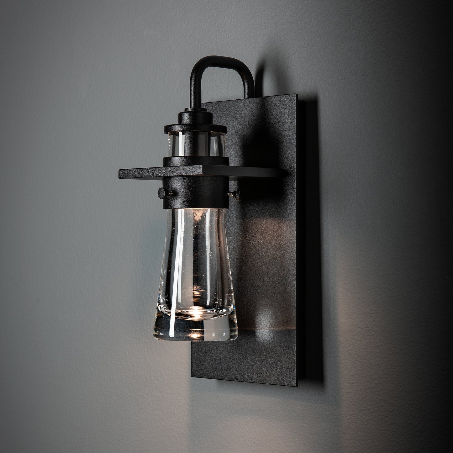 Hubbardton Forge Erlenmeyer Medium Outdoor Sconce with black base and clear glass shade, handcrafted American lighting accent for outdoor spaces.