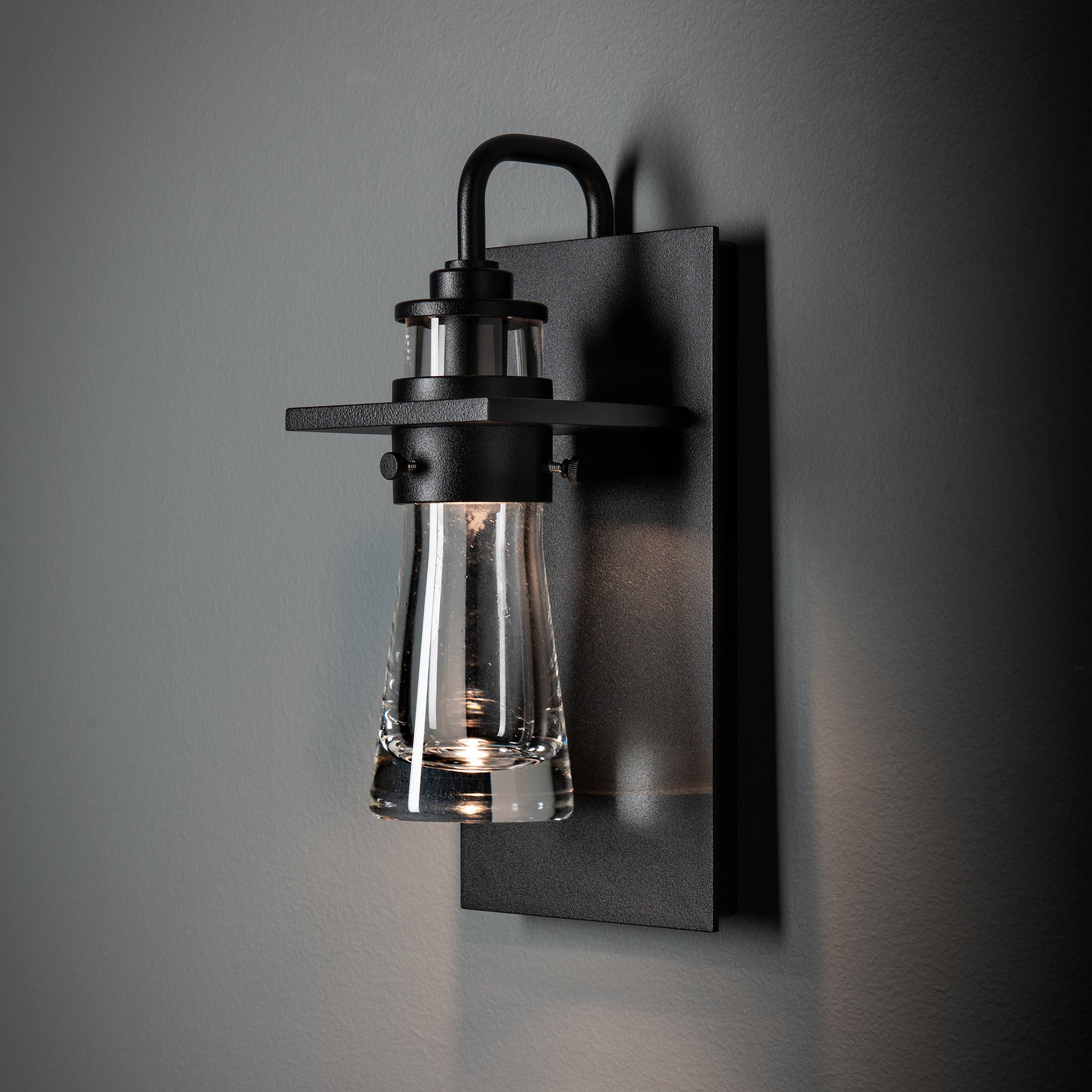 Hubbardton Forge Erlenmeyer Medium Outdoor Sconce with black base and clear glass shade, handcrafted American lighting accent for outdoor spaces.