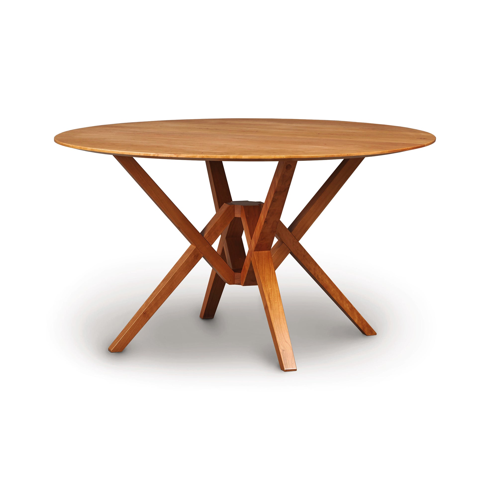 A wooden Copeland Furniture Exeter Round Solid Top Dining Table with a cross-legged base, isolated on a white background.