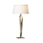 A modern facet table lamp with a sleek, twist-shaped metallic stand handcrafted by Hubbardton Forge and a large, white, cylindrical shade, set against a plain white background.