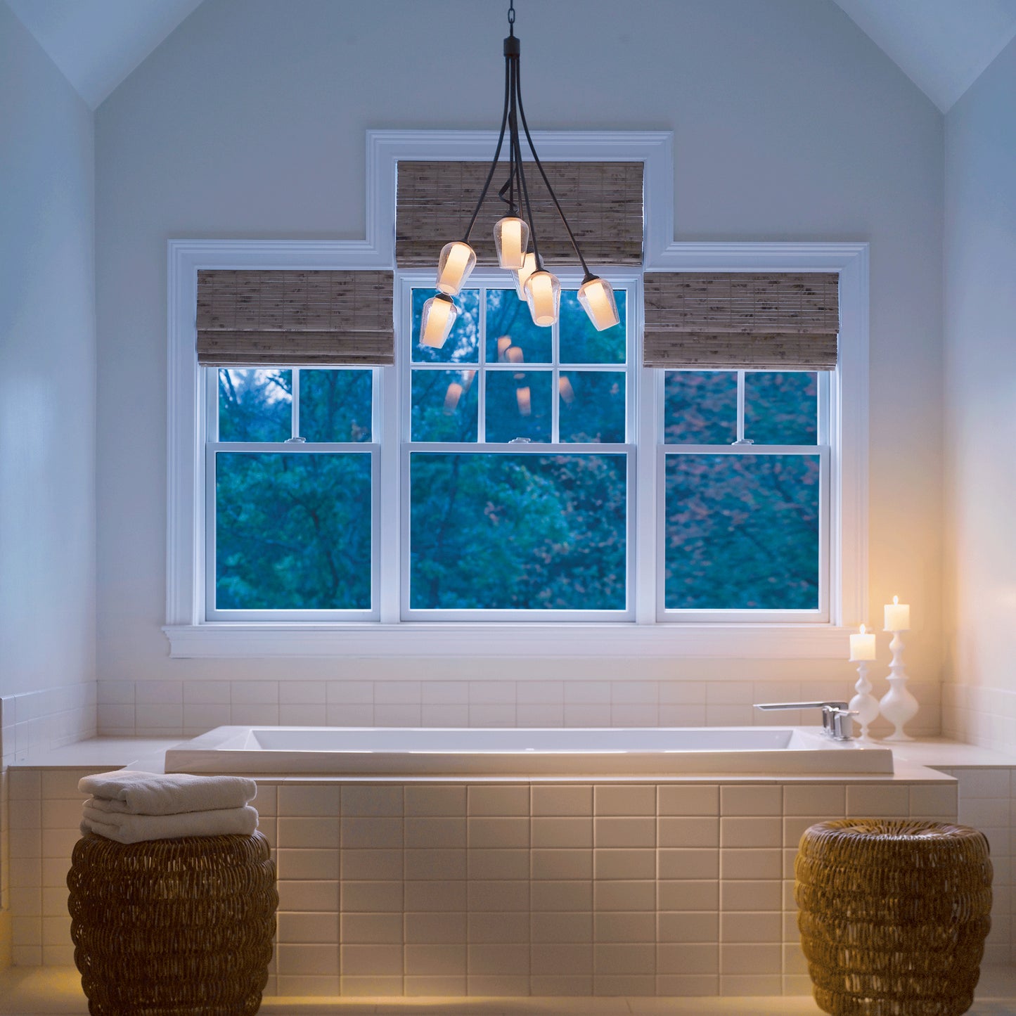 Hubbardton Forge Flora 6-Arm Chandelier hanging over a white bathtub with lit candles on the edge, complemented by elegant wicker side tables.