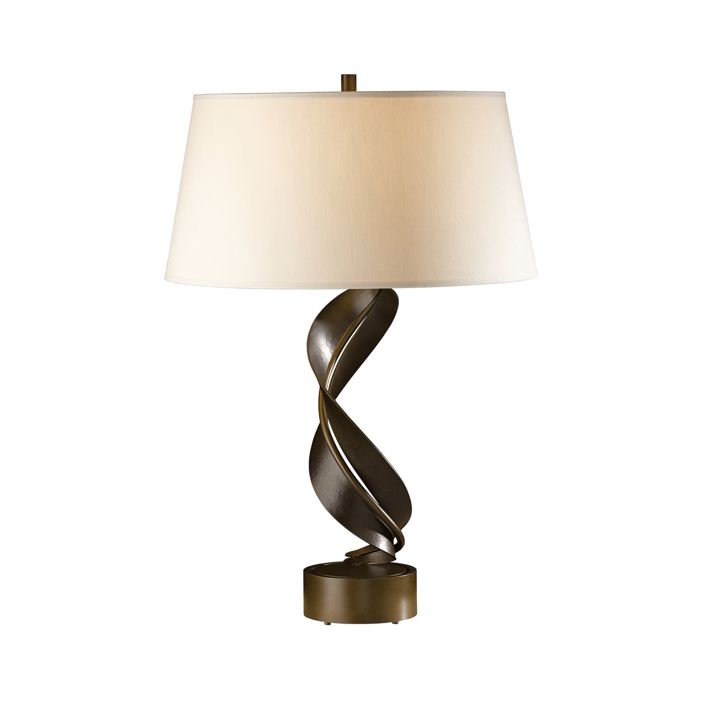 An elegant Hubbardton Forge Folio table lamp featuring a spiraling hand-forged wrought iron base and a wide, off-white lampshade, emitting a warm, inviting glow.