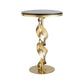 A small, round Folio Wood Top Accent Table from Hubbardton Forge features a black surface and is supported by a gold metal base with a twisted design. The base, finished in modern brass, stands on a circular gold platform, effortlessly blending modern and elegant elements.