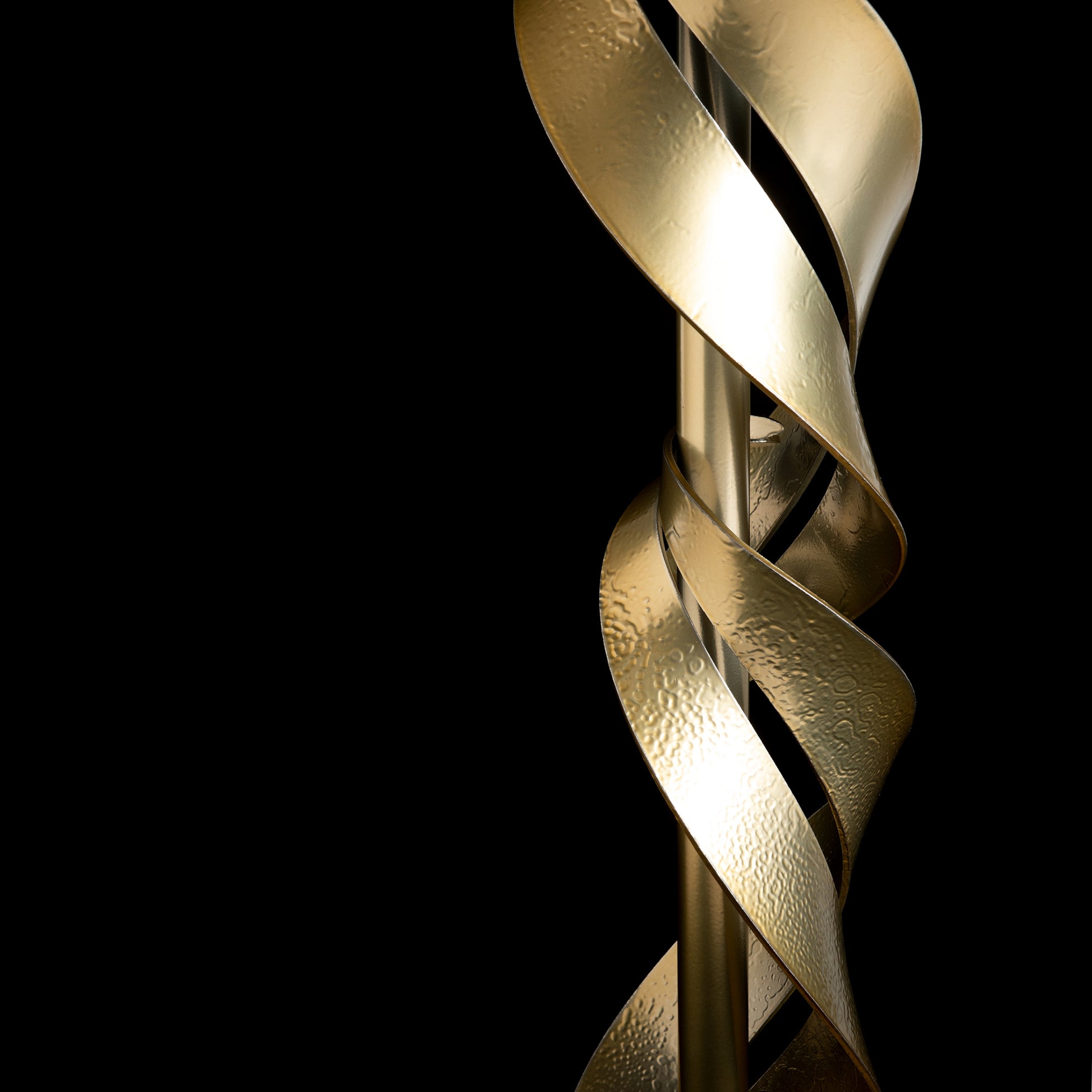 Close-up of a spiraling, textured sculpture in the style of Hubbardton Forge's Folio Wood Top Accent Table against a black background. The elegant design wraps around a vertical pole, showcasing its dynamic and modern brass finish.