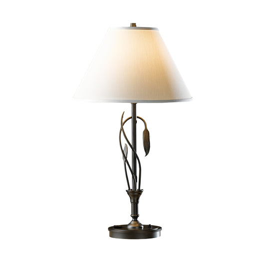 A hand-crafted Forged Leaves and Vase Table Lamp by Hubbardton Forge, this table lamp features a white shade on it.
