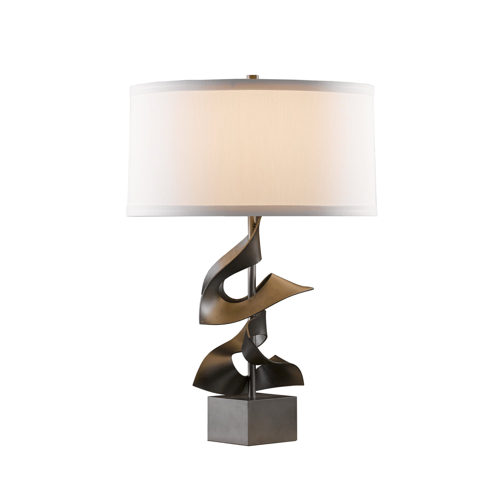 A modern Hubbardton Forge Gallery Two Fold Table Lamp with a sculptural metallic base featuring abstract curves, topped with a white cylindrical shade. The lamp is set against a neutral background.