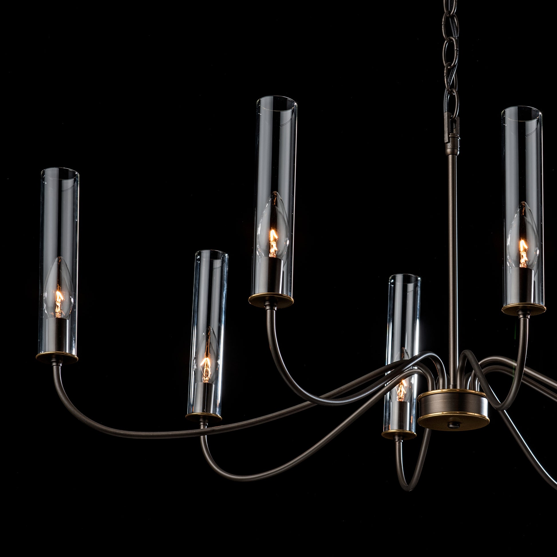 An artisan-crafted Grace 8-Arm Chandelier by Hubbardton Forge, featuring five glass cylinders, suspended elegantly against a contrasting black background.