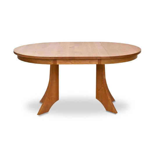 An oval-shaped solid wood Hampton Split Pedestal Extension Table by Lyndon Furniture is shown, featuring a minimalist design with two curved, sturdy legs. The smooth surface and natural wood finish highlight the elegance of this handcrafted American-made furniture piece, perfect for any dining room. This table embodies the charm of high-quality Vermont-made furniture and is available in cherry, walnut, maple, and other hardwoods.