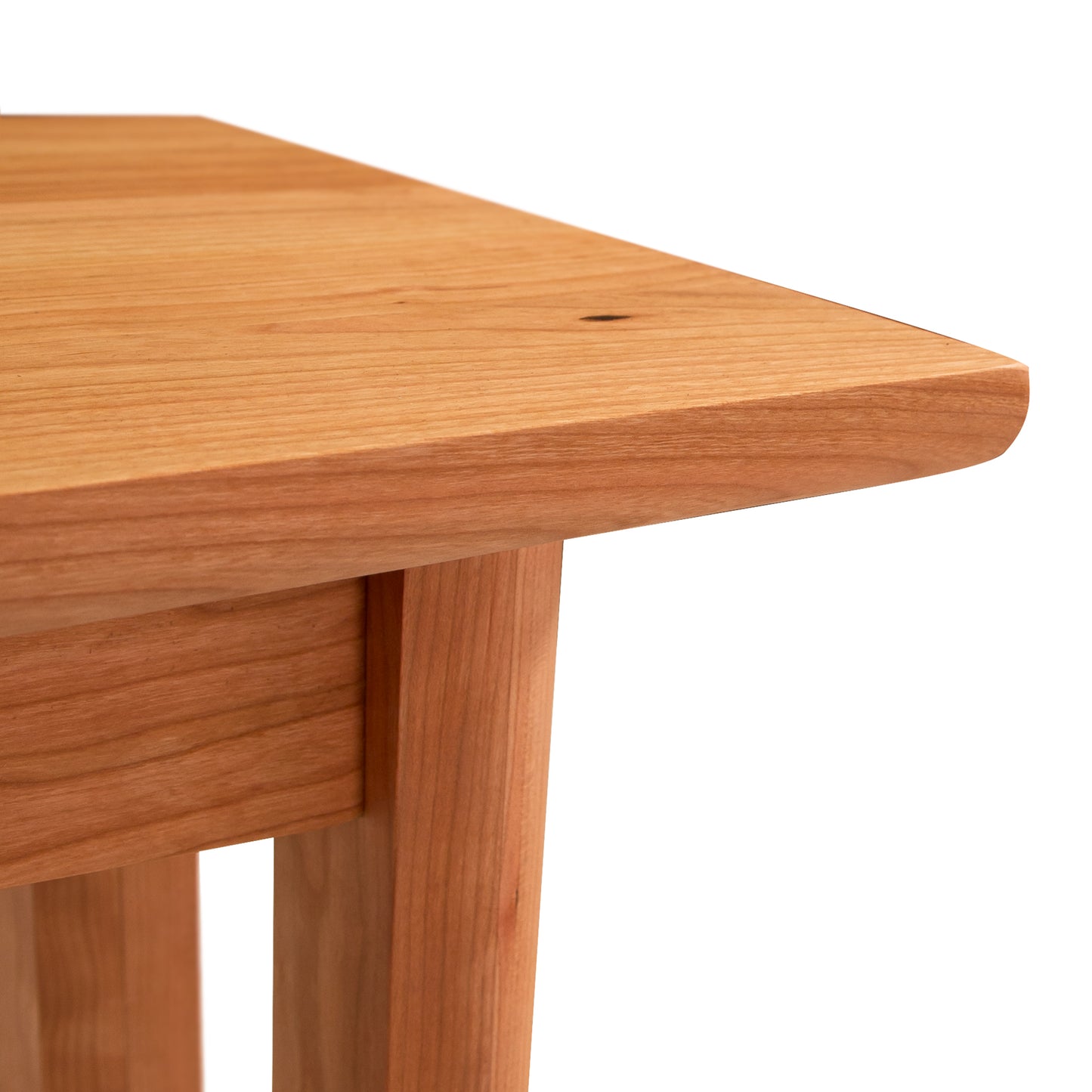 Corner of a Vermont Furniture Designs Heartwood Shaker Bench showing the seat and the top part of a leg, against a white background.