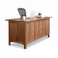 Heartwood Shaker Executive Desk by Vermont Furniture Designs features classic craftsmanship and is paired with a chair, laptop, and books.