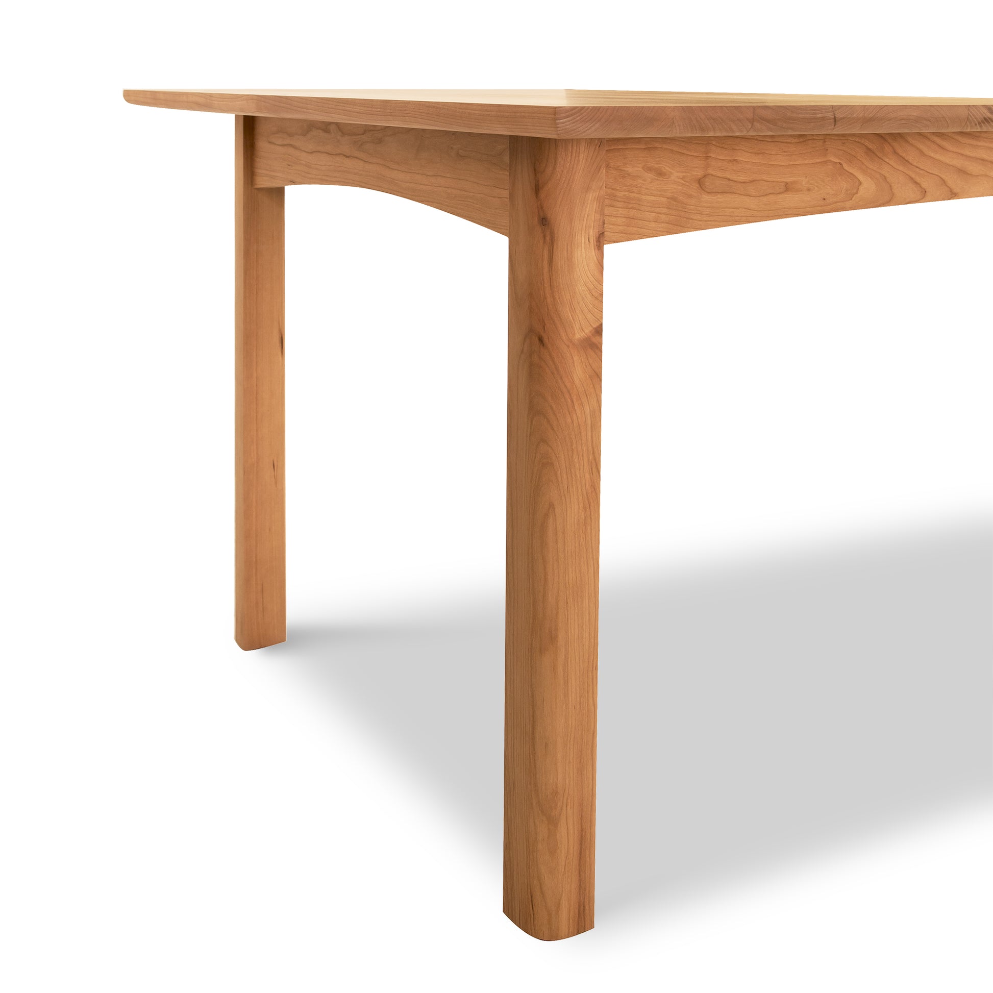 A wooden table with a simple design, featuring one visible leg and a top with a clear wood grain pattern, against an off-white background. This is the Vermont Furniture Designs Heartwood Shaker Extension Dining Table.