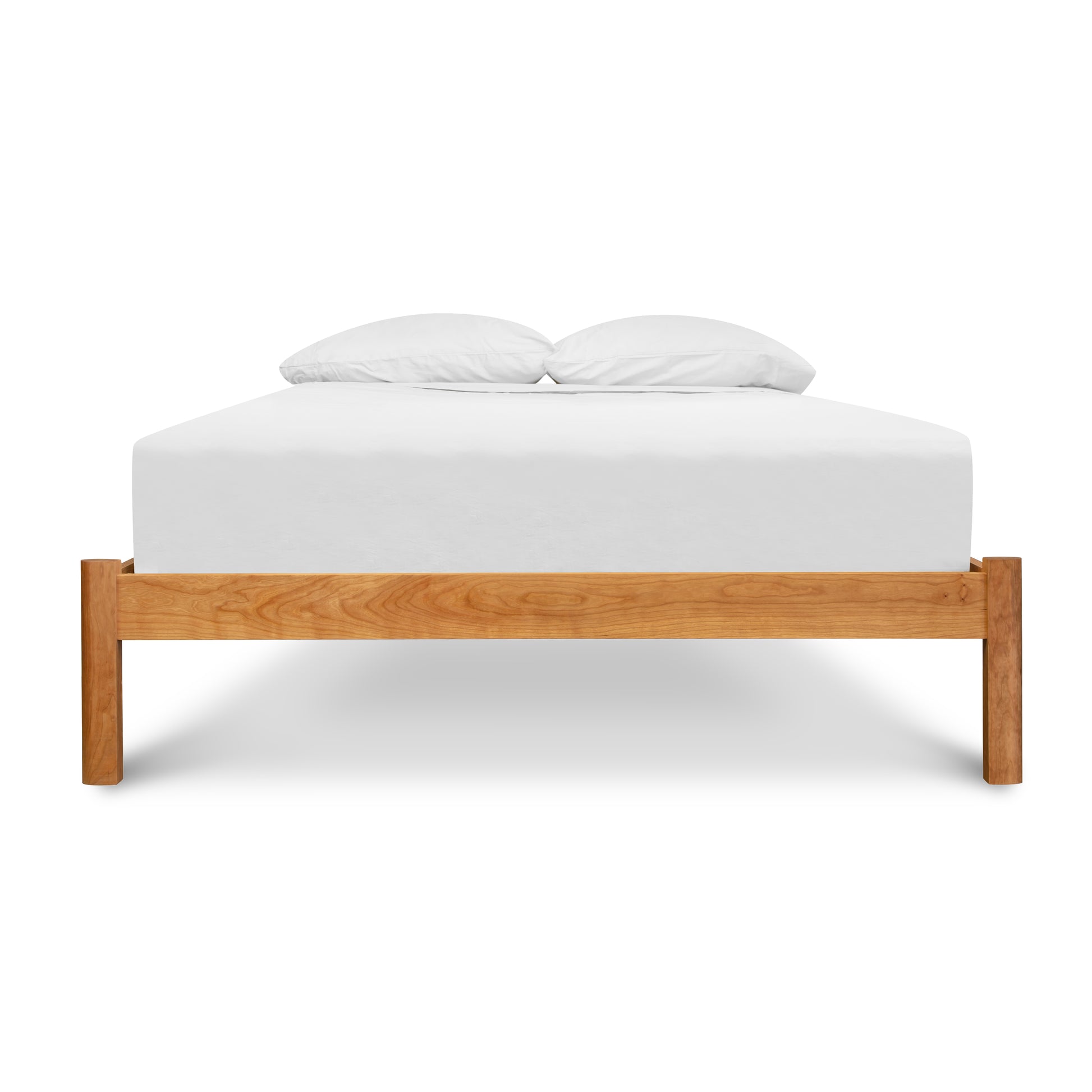 A Heartwood Shaker Studio-Style Platform Bed from Vermont Furniture Designs with a white mattress and two pillows against a white background, complete with an eco-friendly oil finish.
