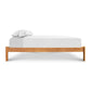 A Heartwood Shaker Studio-Style Platform Bed from Vermont Furniture Designs with a wooden frame and white bedding, isolated on a white background.