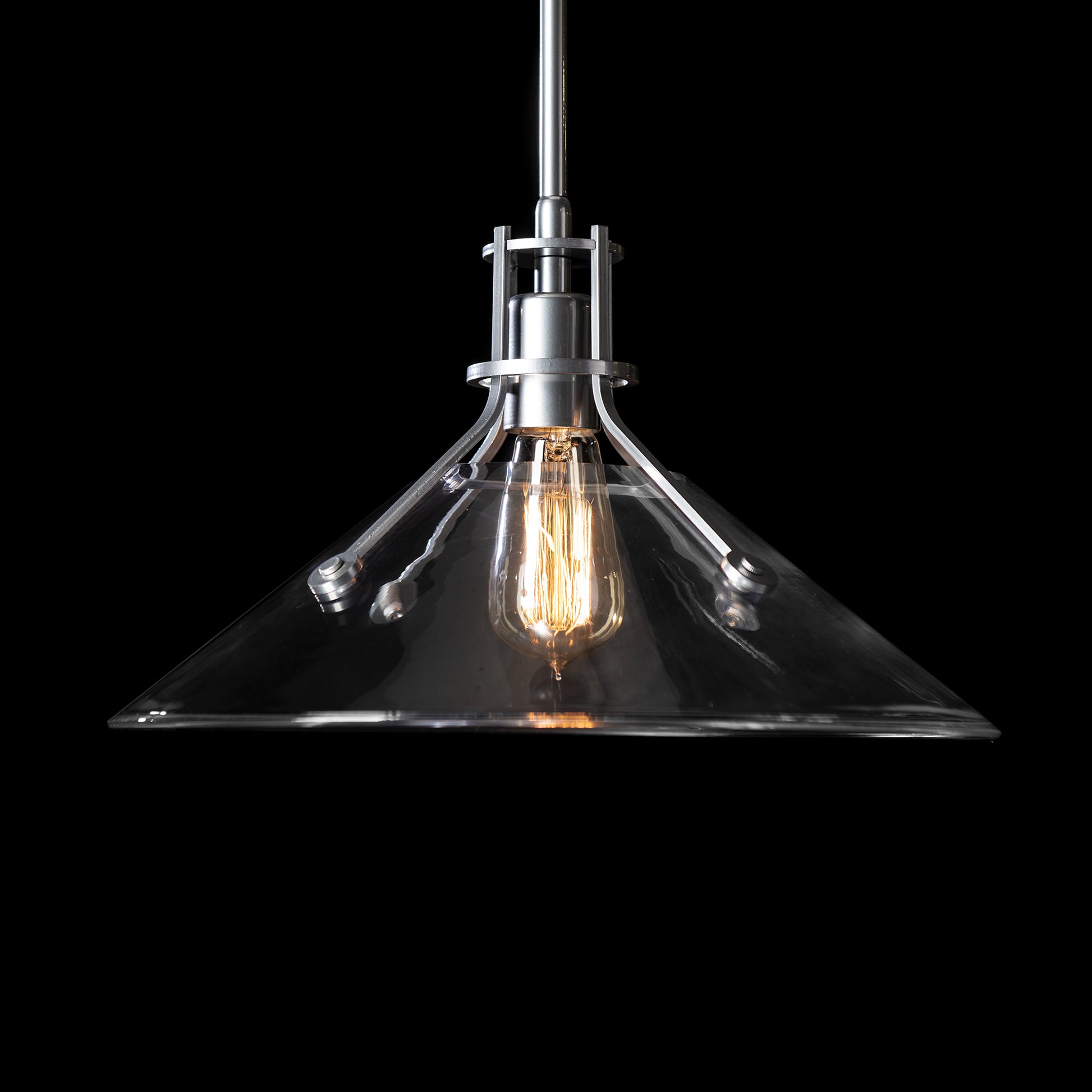 A Hubbardton Forge Henry Medium Glass Shade Pendant with a black background featuring a glass shade and modern industrial styling.