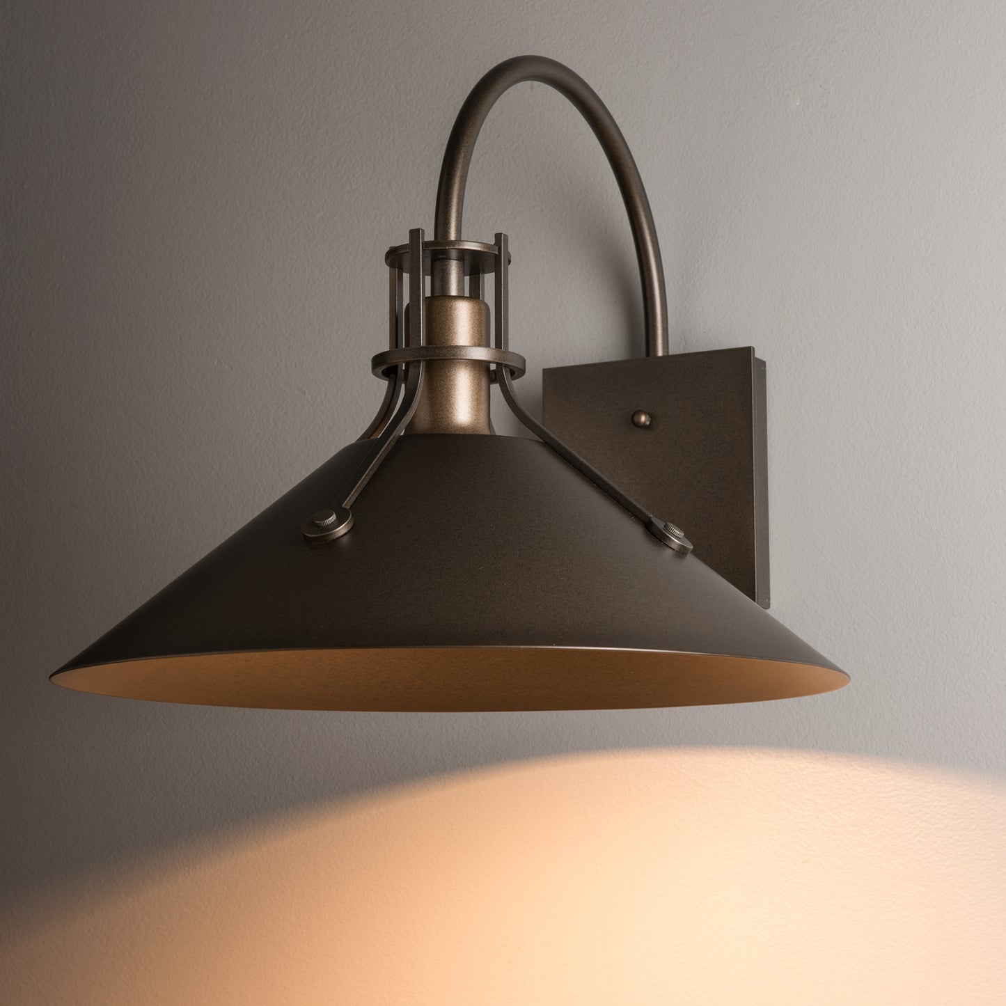 The Henry Large Dark Sky Friendly Outdoor Sconce by Hubbardton Forge features a wide, artisan-crafted conical shade, casting warm light.