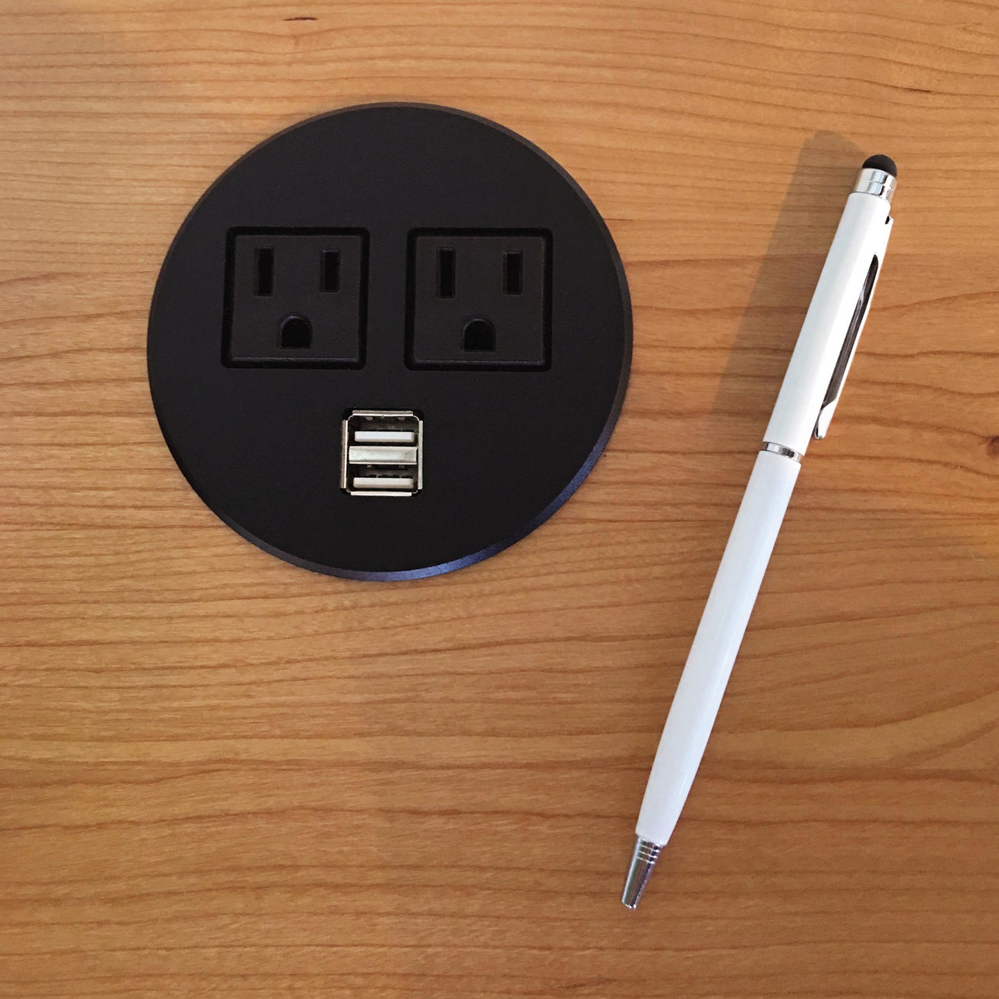 Copeland Furniture Invigo Sit-Stand Desk with embedded black circular power outlet featuring two sockets and USB ports, accompanied by a white pen.