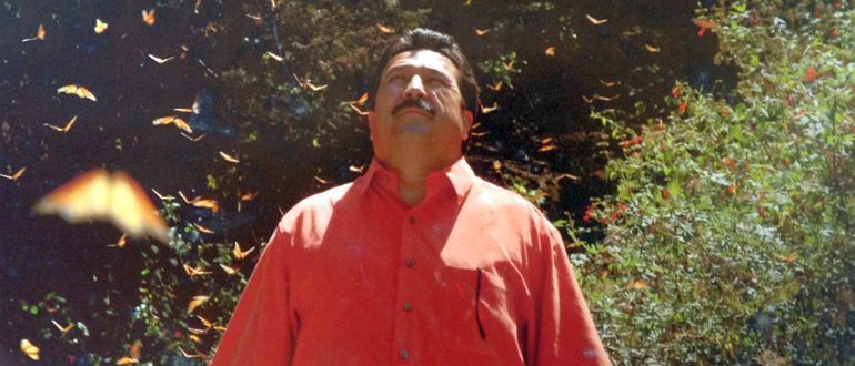 A man in an orange shirt with butterflies flying around him.