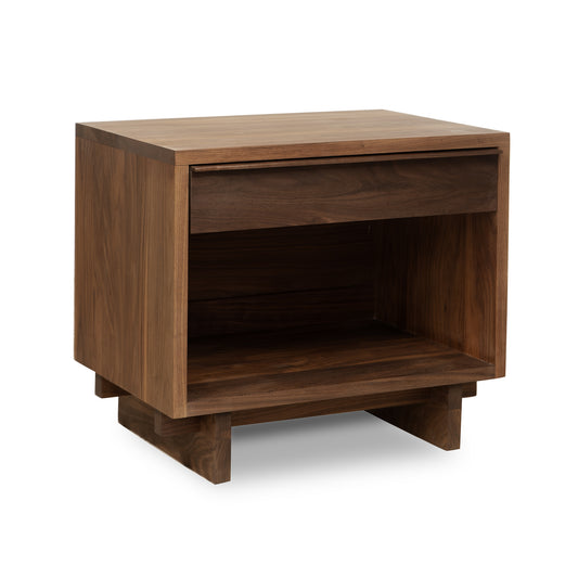 The image shows the Kipling 1-Drawer Enclosed Shelf Wide Nightstand by Vermont Furniture Designs, featuring a single top drawer and an enclosed shelf below, perfectly complementing the natural walnut finish of the Kipling Platform Bed. The nightstand boasts clean lines and a minimalist design, supported by four short, sturdy legs. The wood has a smooth finish and a rich, natural color.